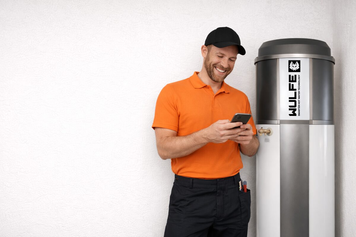 A plumber using the ACTIV8 app on his phone next to a Wulfe heat pump unit